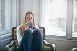 Woman drinking tea in a comfy chair by the window.