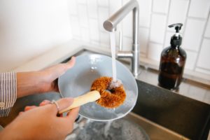 person uses scrub brush to wash dishes under a faucet of running water