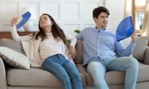 couple sits on couch fanning themselves